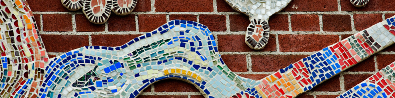 Close-up of a large colourful mosaic installed on an exterior brick wall, depicting abstract shapes and floating milkweed pods.