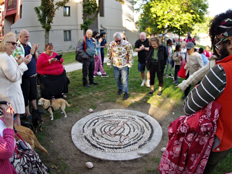 A crowd of people celebrate the unveiling of a pebble mosaic in a park.
