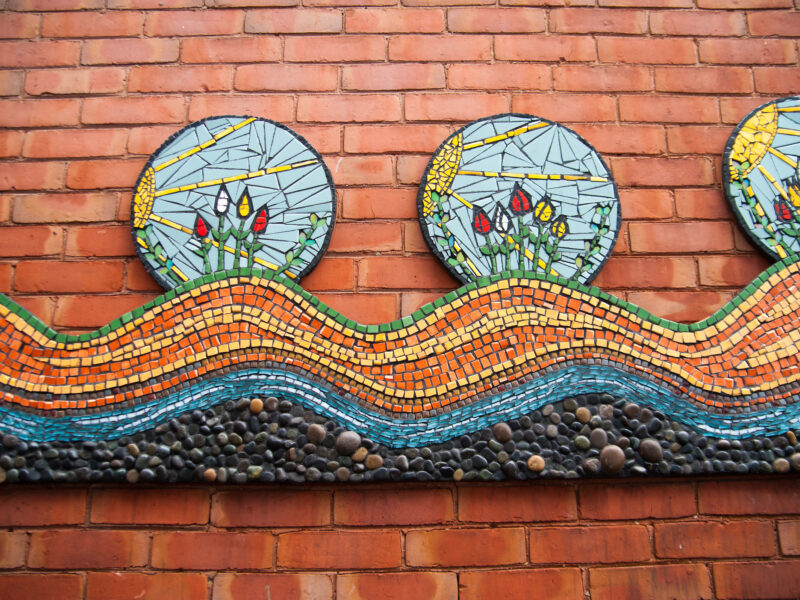 Photo of a mosaic that contains three separate scenes of blossoming flowers all connected by a long, curved mosaic bottomed with pebbles that mimics a water system.