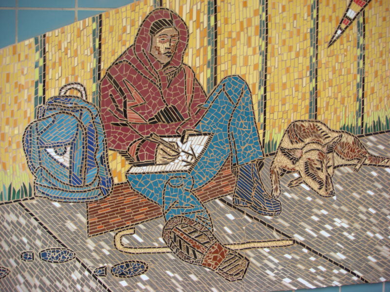 Mosaic depicting a person and dog, sitting on the sidewalk with a backpack, notebook, and walking cane.