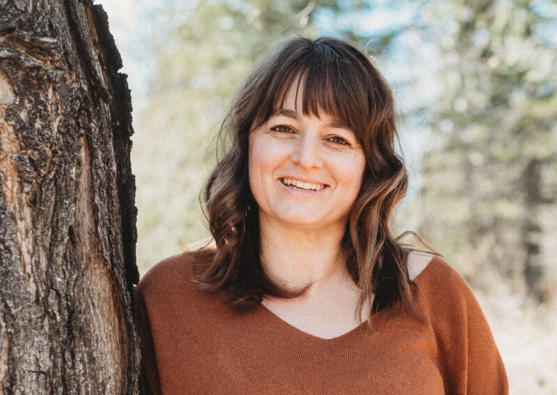 headshot of a smiling woman standing outdoors beside a tree
