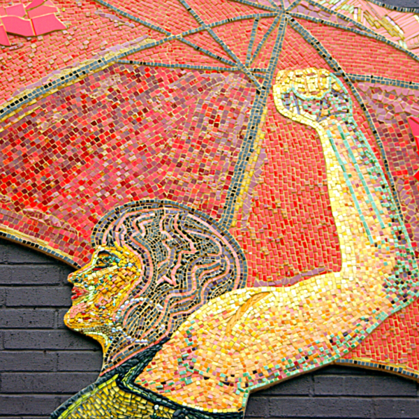 A close-up photo of a mosaic containing a woman’s head, arm and fist, and a red umbrella.