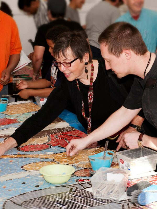 A group of people work around a table on a large ceramic mosaic.
