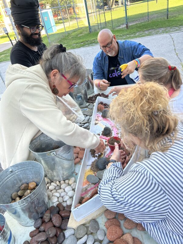 People surround a table covered in stones, creating a pebble mosaic.