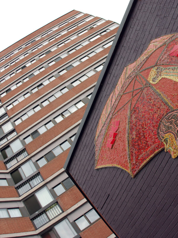 A large mosaic mural depicts a woman holding a red umbrella. A tall condo building in the background towers over the mosaic.