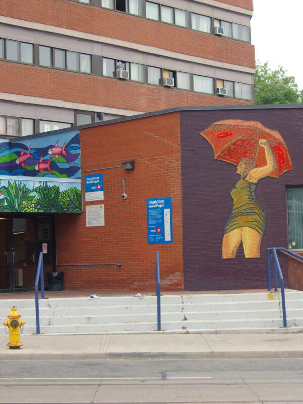 A large mosaic of a woman holding a red umbrella is installed next e to a condo building’s entrance.