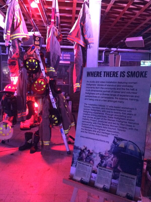 An art installation of firefighter uniforms and gear hung on a ladder next to an exhibition didactic.