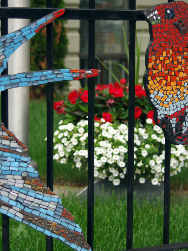 Close-up of two ceramic mosaic birds attached to an iron fence.