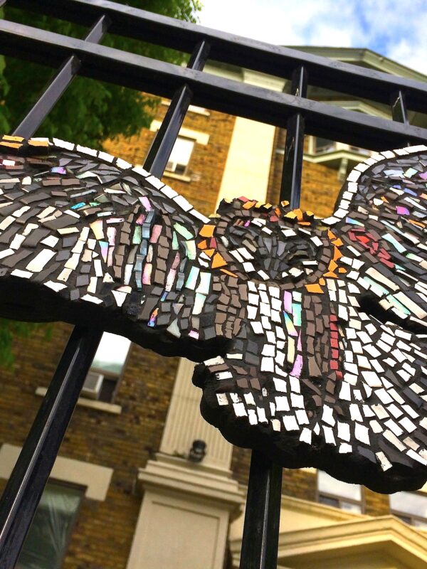 Close-up of a ceramic mosaic owl attached to an iron fence.