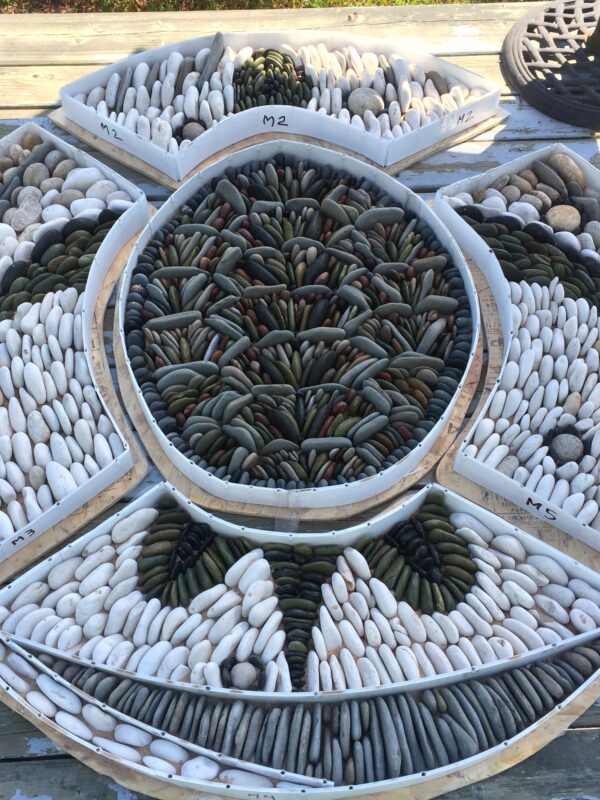 Pieces of a large pebble mosaic fit together to depict a turtle.