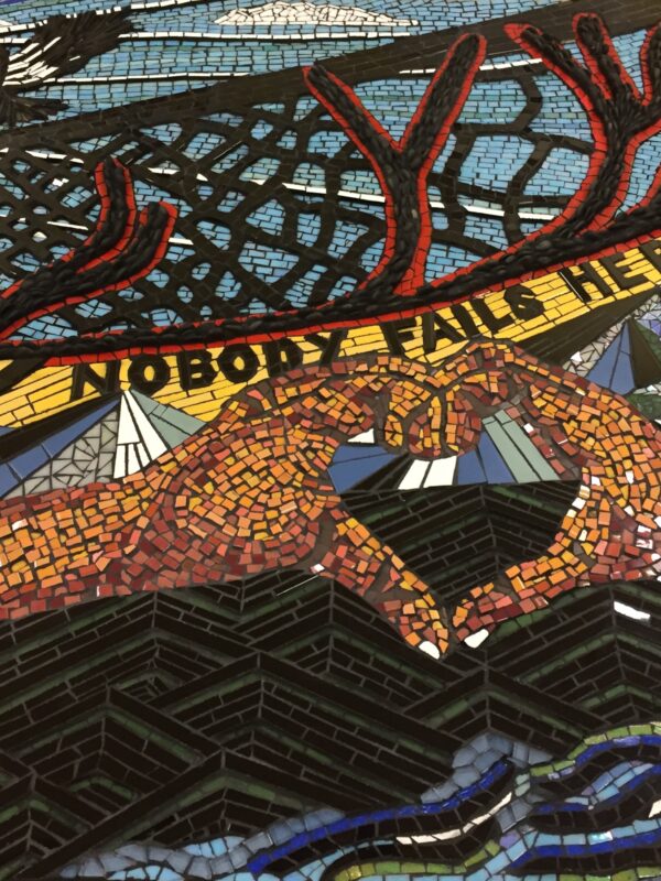 Close-up of a colourful mosaic depicting hands forming the shape of a heart with interwoven text that reads, “nobody fails here”.