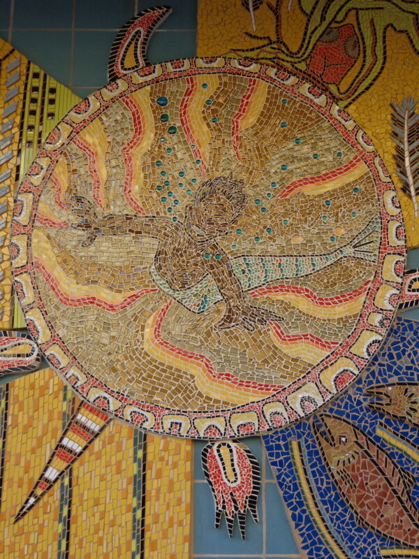 Large mosaic installed on a wall depicting a turtle, a merperson, salmon, a human in a forest, and a cityscape covered in butterflies.