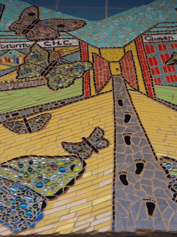 Colourful mosaic depicting a walking path in a city, surrounded by buildings and butterflies. Text on buildings reads, “Central Toronto C.H.C., Queen W”.