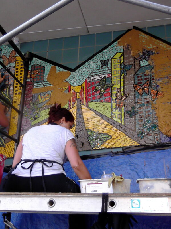 Three people on scaffolding installing a large mosaic onto a wall.