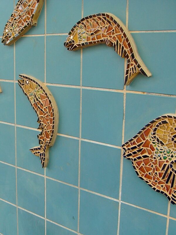 Multiple small mosaics in the shape of salmon decorate a blue tiled wall.