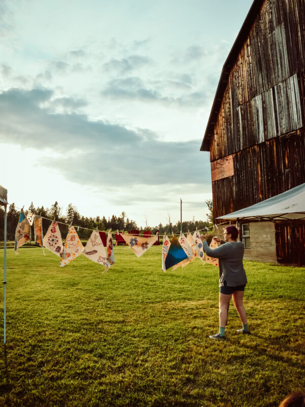 A person hanging prints to dry on a clothesline in front of a barn and sun set.