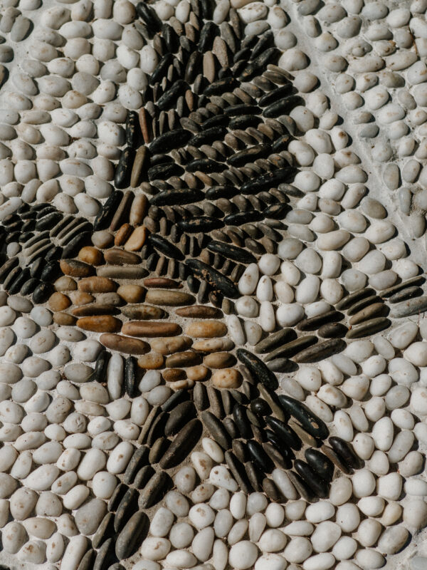 Close-up of a pebble mosaic. The mosaic design includes a chickadee made up of brown, black, and grey stones.