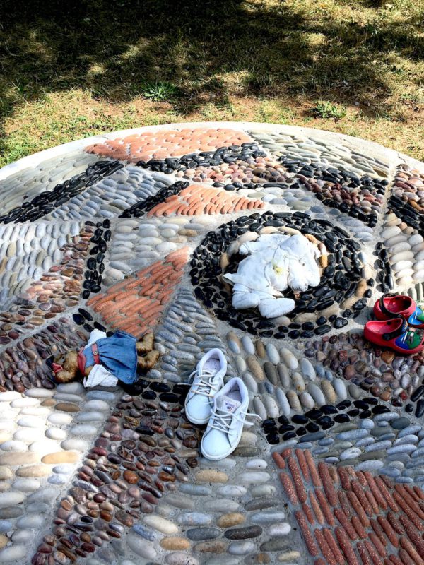 Photo of a pebble mosaic. Childrens toys and shoes are laid upon it.