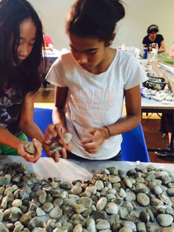 Two teens select stones from a pile on a table.