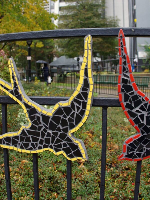 Close-up of two small ceramic birds attached to an iron fence.