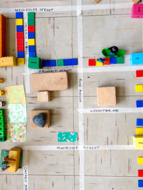 A neighbourhood mapped out on the ground with tape, building blocks and other toys.