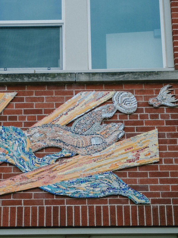 A large colourful mosaic installed on an exterior wall depicting a person’s hand.