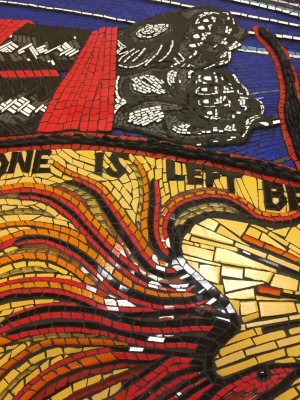 Close-up of a colourful mosaic depicting arms tied with rope. Text reads, “no one is left behind”.