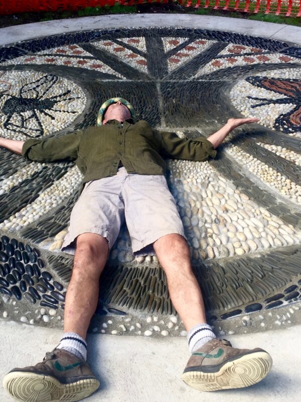 A person lays on their back on a large pebble mosaic, arms outstretched to their sides.
